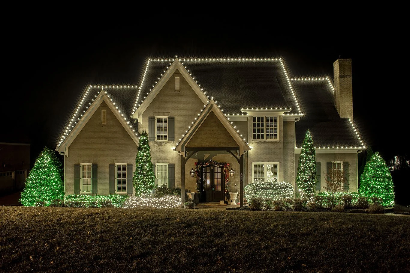 Home with professional warm white Christmas roofline lighting and lit shrubs.